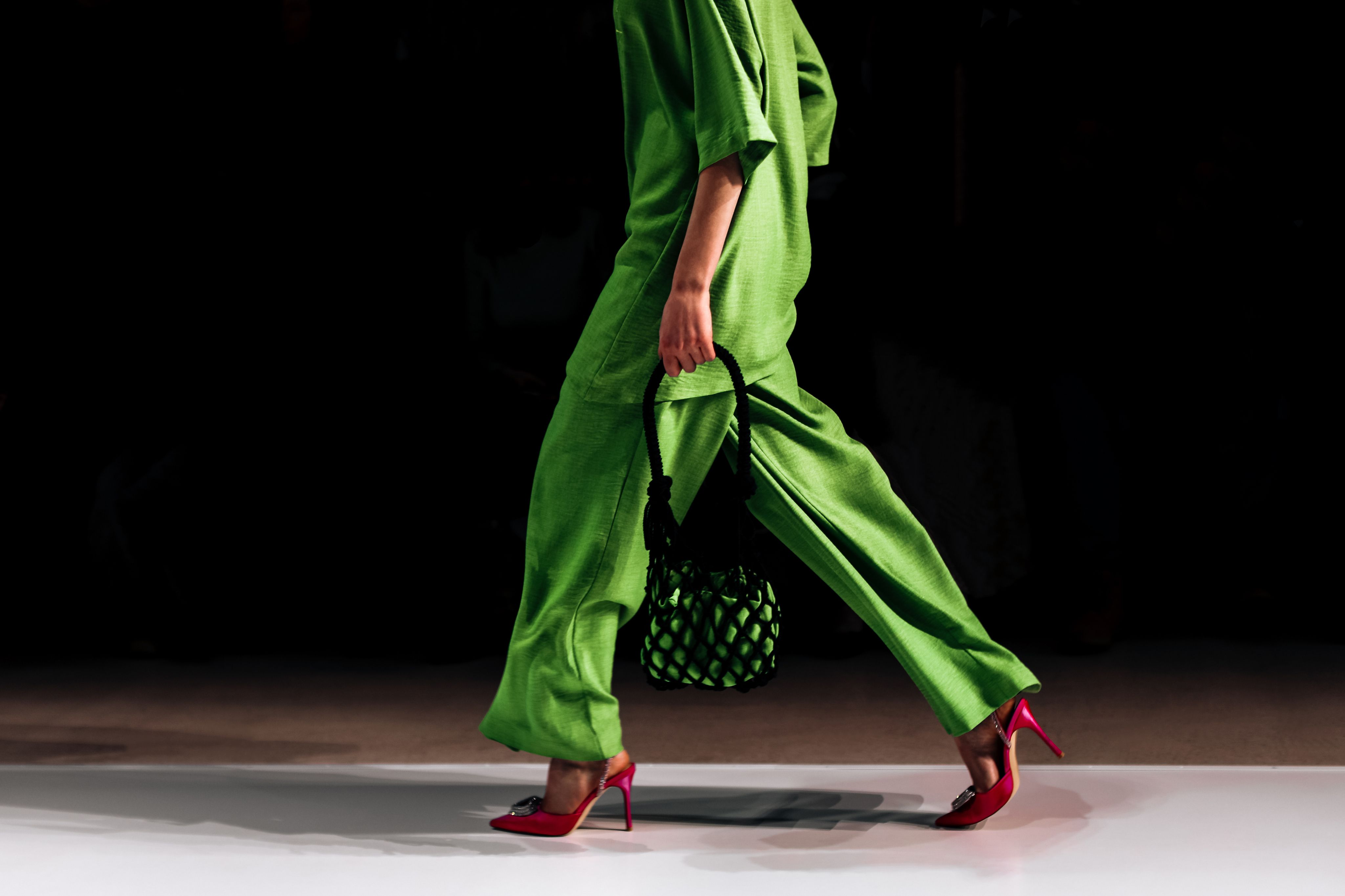 Model im leuchtend grünen Outfit und roten High Heels geht auf dem Laufsteg.