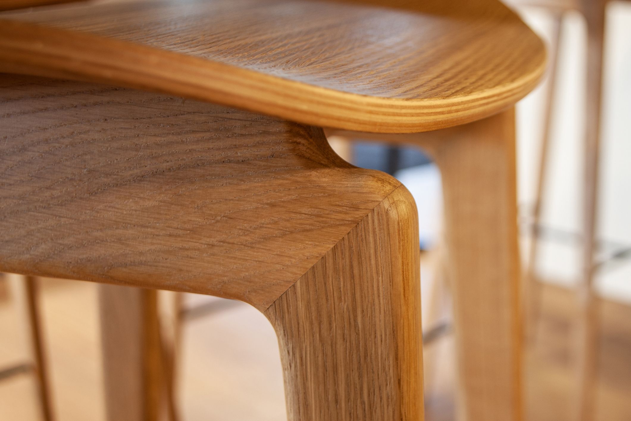 Nahaufnahme eines hellen Holzhockers mit sichtbarer Maserung und geschwungenem Design. Der Fokus liegt auf der Verbindung von Sitzfläche und Bein.